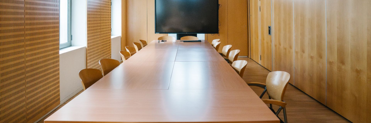Salle de réunion avec table, chaises, écran et armoires.