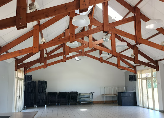 Salle avec poutres apparentes, ventilateurs, tables pliantes et porte.