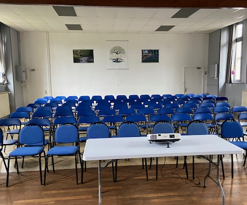 Salle de conférence avec tables, chaises, ordinateur, écran et projecteur.