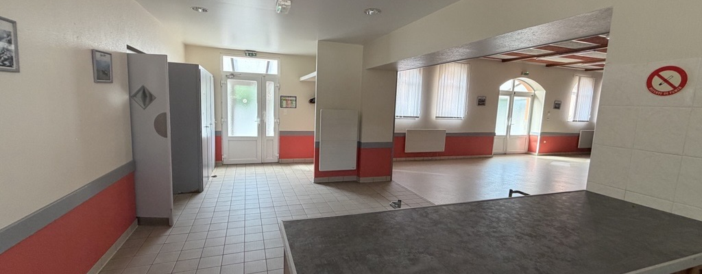 Salle avec table, frigo, étagères, portes et fenêtres.