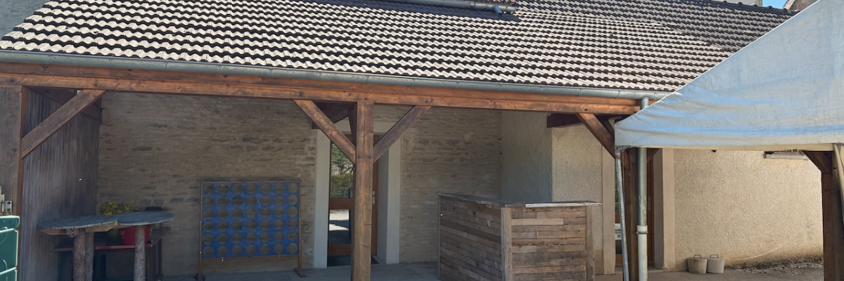 Bâtiment avec toit en tuiles, structure en bois, table, étagère, et clocher en arrière-plan.