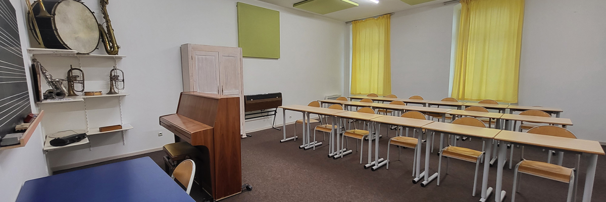 Salle de classe avec piano, instruments, bureaux, chaises, tableau et rideaux.