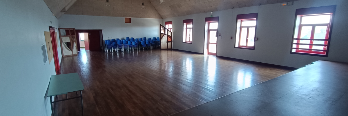 Salle vide avec parquet, chaises alignées, fenêtres, portes et table basse.