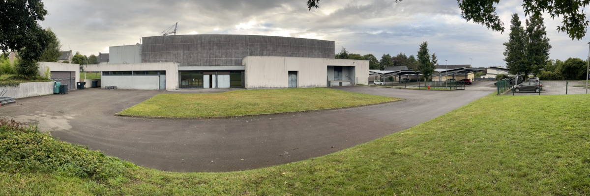 Bâtiment d'apparence industrielle avec des portes de garage, stationnement et verdure environnante.