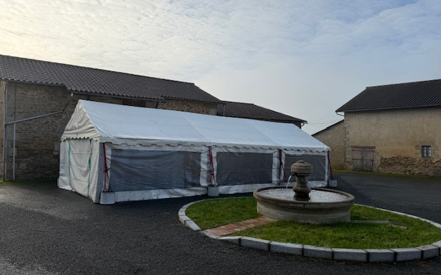 Tente blanche près de bâtiments anciens, fontaine au premier plan.