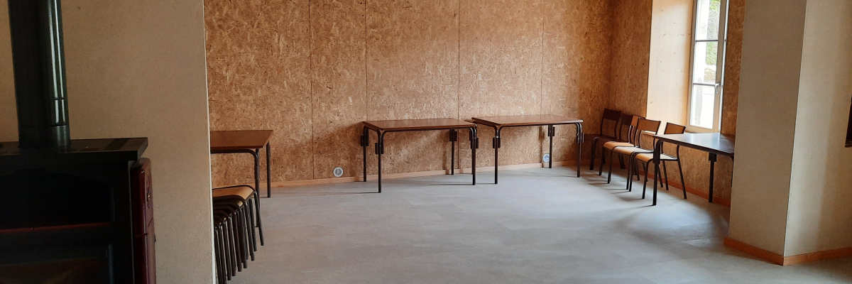 Pièce avec tables, chaises, poêle à bois et fenêtre.