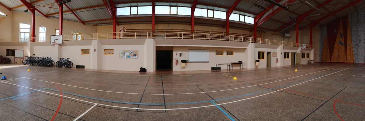 Gymnase avec vélos, table, tableau blanc, mur d'escalade et terrain de basket.