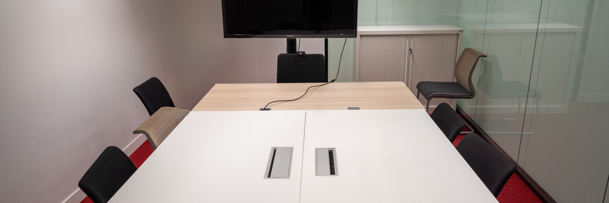 Salle de réunion avec table, chaises, écran, télécommande et armoire.