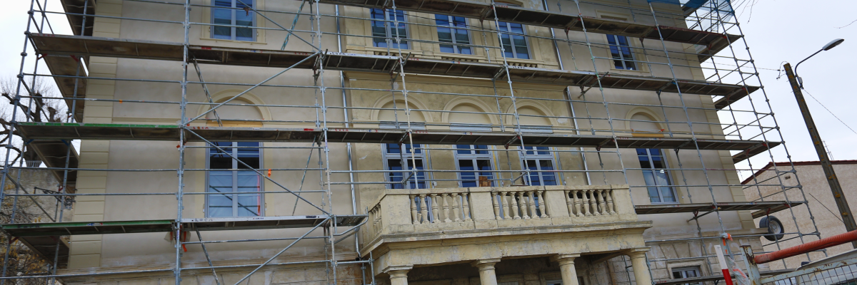 Bâtiment en rénovation avec échafaudages, fenêtres et balcons.