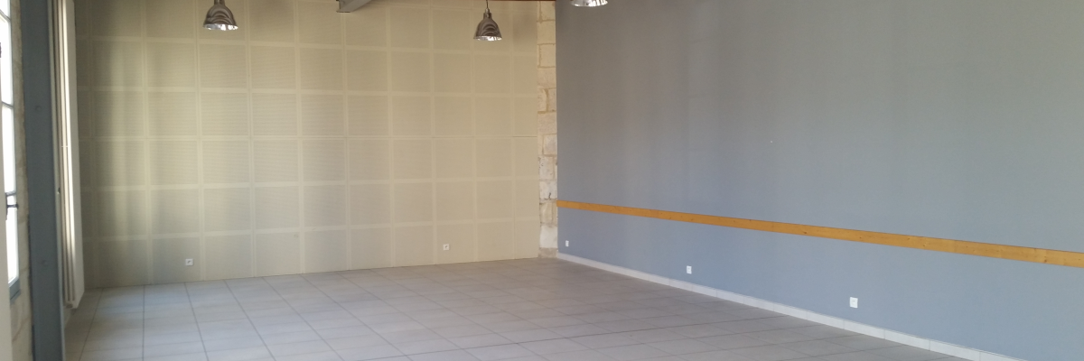 Pièce vide avec carrelage, murs peints, plinthes, prises électriques, interrupteurs, plafond avec poutres apparentes et suspensions.