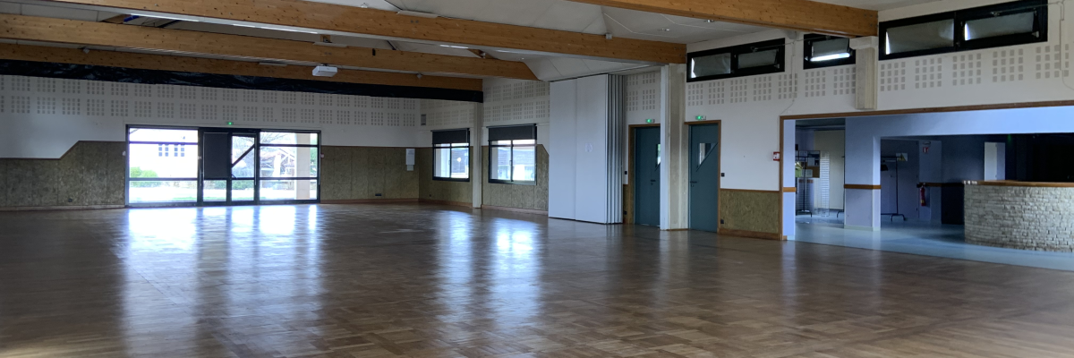 Salle spacieuse avec parquet, poutrelles apparentes, portes, fenêtres et distributeurs automatiques.
