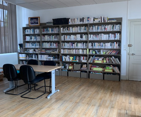 Bibliothèque avec étagères de livres, bureau, deux chaises et porte.
