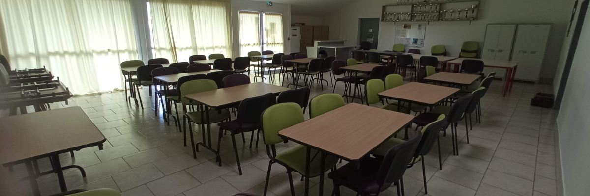 Salle avec tables, chaises, armoires, projecteur et machine à café.