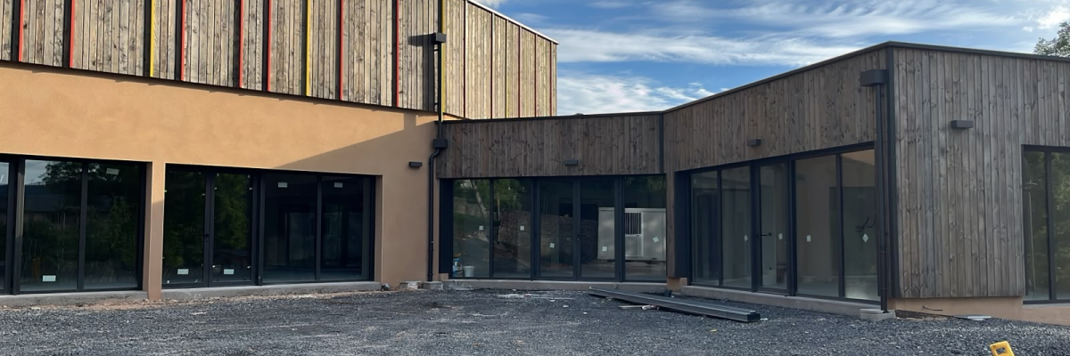 Bâtiment moderne avec façade en bois et verre, parking graviers.