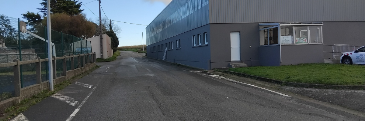 Route menant à un bâtiment industriel avec clôture, lampadaire et voiture.