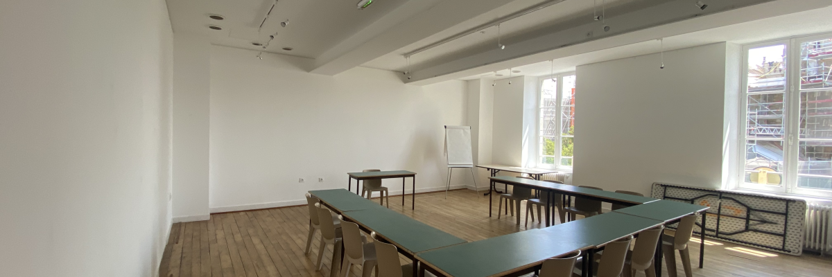 Salle avec tables, chaises, tableau blanc, radiateur et fenêtre.