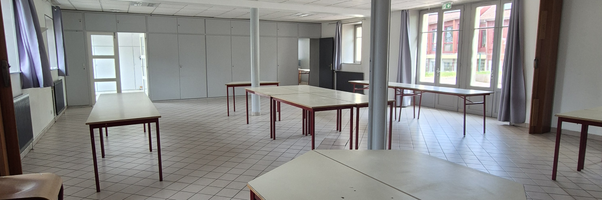 Salle avec tables, chaises, fenêtres et plafond à dalles.