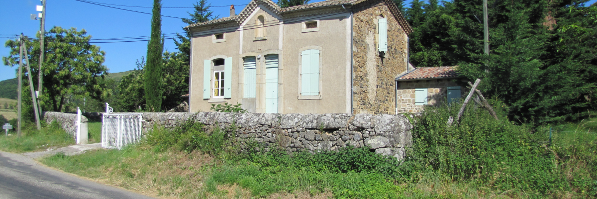 Maison de pierre avec fenêtres blanches, clôture et route.