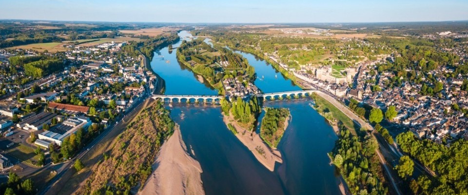 Vue aérienne d'une rivière traversant une ville avec un pont, des bâtiments et des zones vertes.