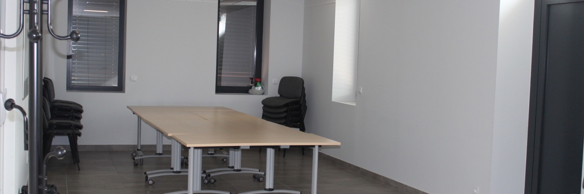 Salle vide avec table, chaises, porte-manteau et issue de secours.