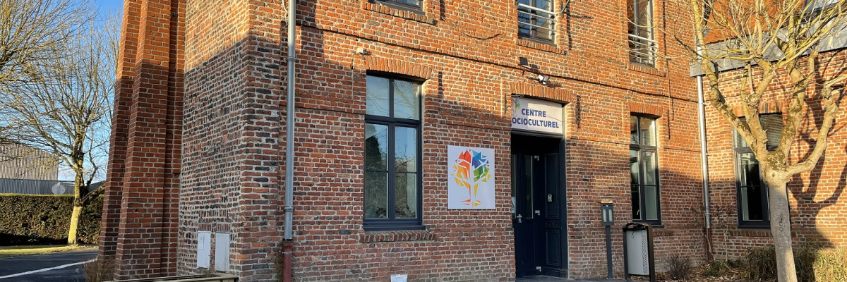 Bâtiment en brique avec entrée, affiche, arbre et parking.