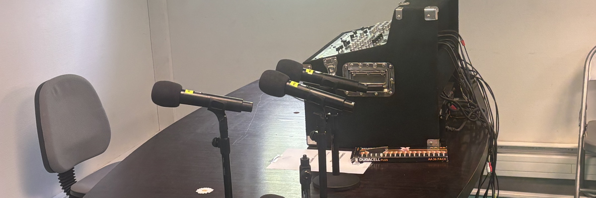 Studio d'enregistrement avec table de mixage, microphones, chaises et câbles.