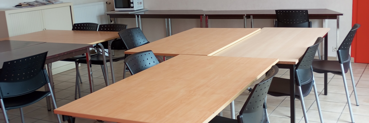 Salle avec tables, chaises, poste de travail surélevé et porte rouge.