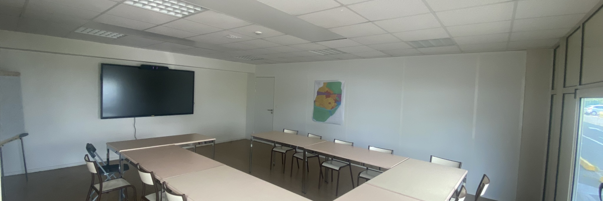 Salle avec tables en U, chaises, écran et tableau.