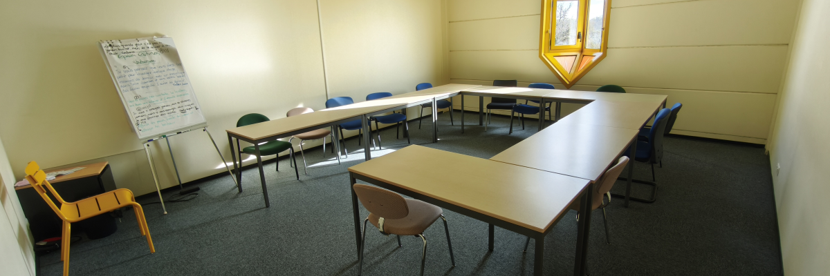 Salle avec tables, chaises, tableau blanc et fenêtre.