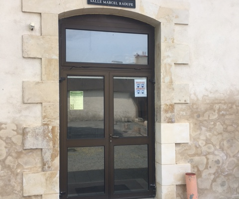 Entrée avec porte vitrée, paillasson, extincteur et enseigne.