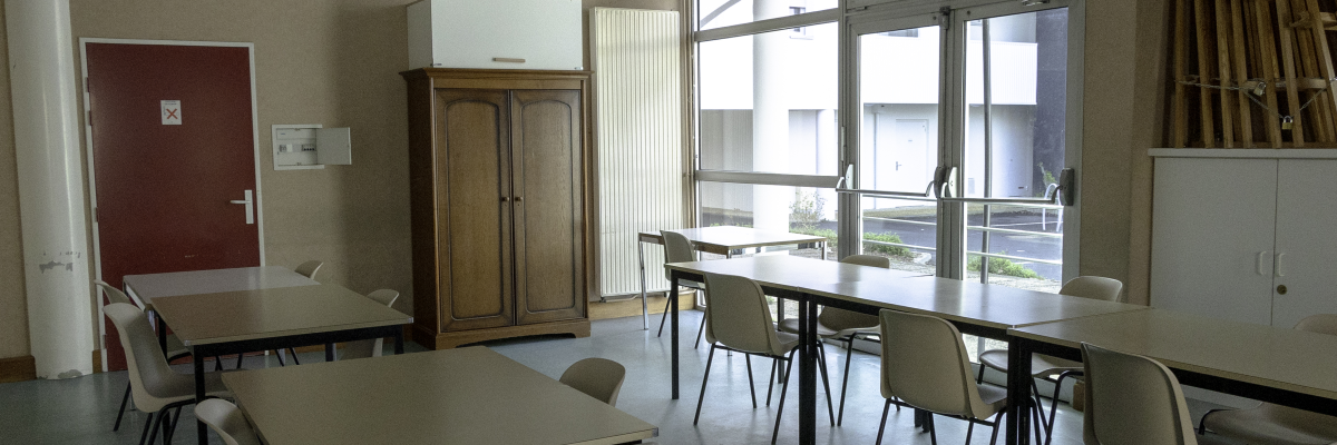 Salle avec tables, chaises, armoire, porte rouge et fenêtre.