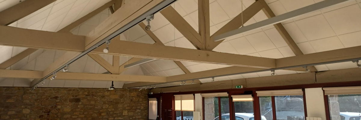 Salle avec grandes fenêtres, murs en brique, poutrelles apparentes, éclairage suspendu.