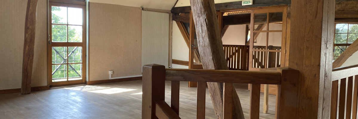 Pièce avec sol en bois, rambarde en bois, fenêtres et escalier.