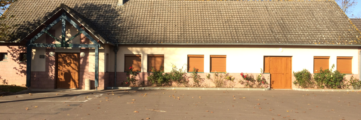 Bâtiment avec toit en tuiles, portes et fenêtres en bois, parking vide.