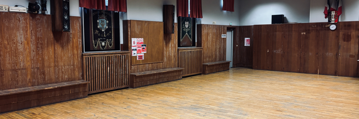Salle avec parquet, bancs, haut-parleurs, rideaux, radiateur, affiches et portes.