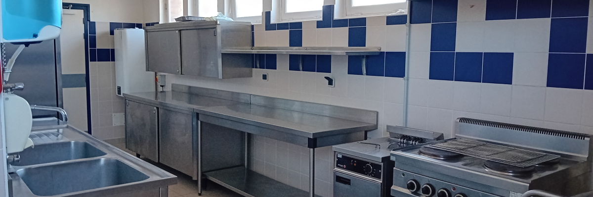 Cuisine équipée avec plans de travail, fours, plaques de cuisson, éviers et étagères.