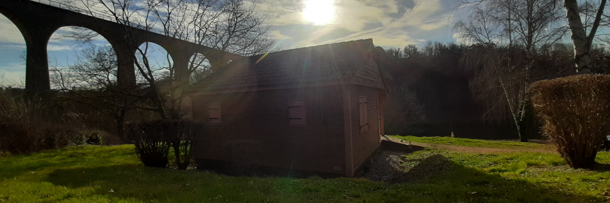Cabane en bois près d'un pont ferroviaire sous un ciel partiellement nuageux.