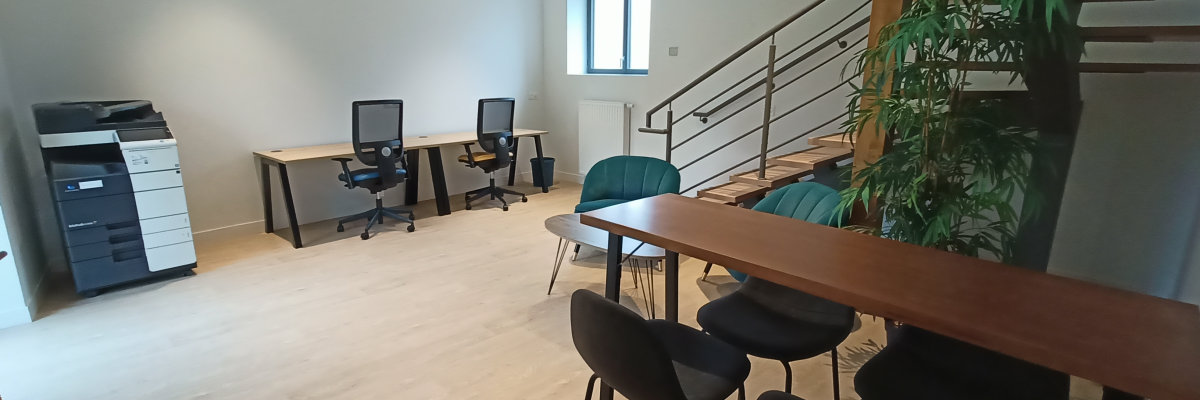 Bureau avec imprimante, trois postes de travail avec écrans et chaises, table avec tabourets, plante, escalier.
