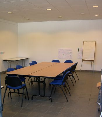Salle avec tables, chaises, tableau blanc et paperboard.