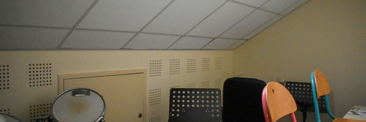 Studio d'enregistrement avec batterie, pupitres, chaises et table de mixage.