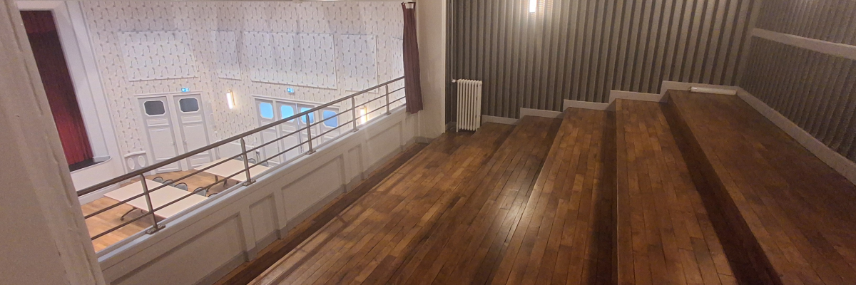 Salle avec parquet, murs de métal, rambarde et portes vitrées.