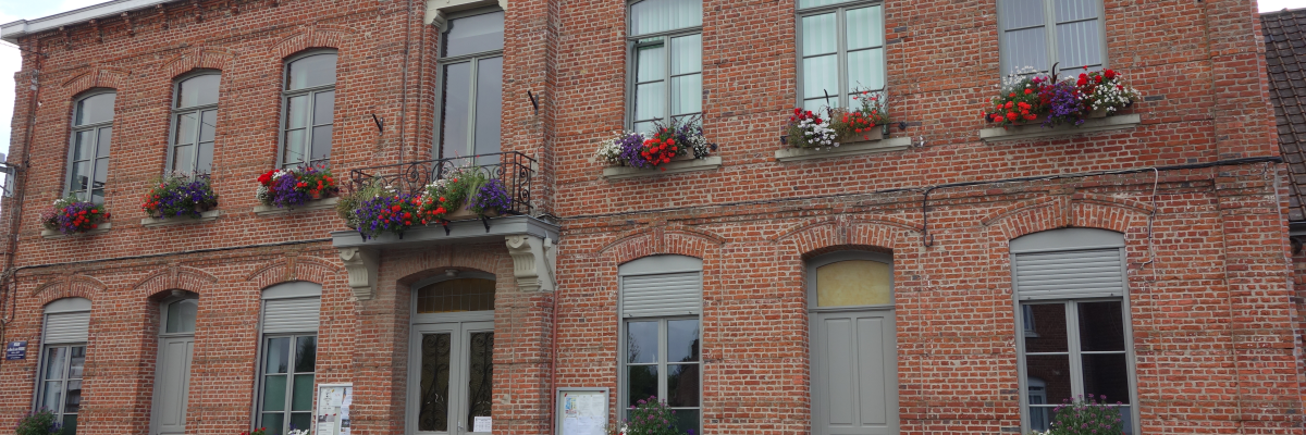 Bâtiment en brique avec horloge, fleurs et portes.