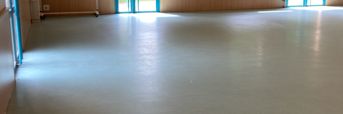 Salle vide avec haut plafond, portes vitrées et sol lisse.