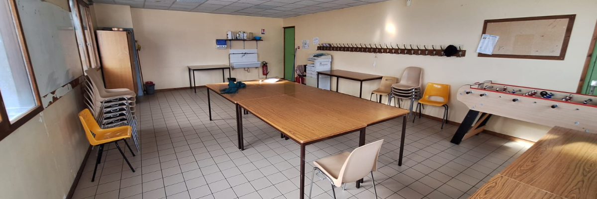 Salle avec tables, chaises, tableau, évier, frigo et machine à café.