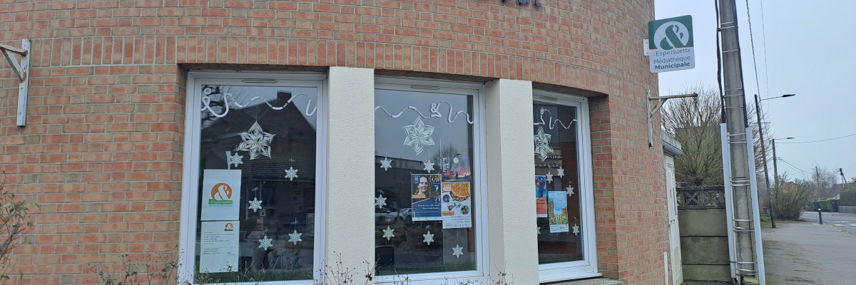 Bâtiment en brique avec enseigne "Espace Culturel Jacques Bout". Fenêtres décorées de flocons de neige et affiches. Boîte aux lettres verte à l'extérieur.