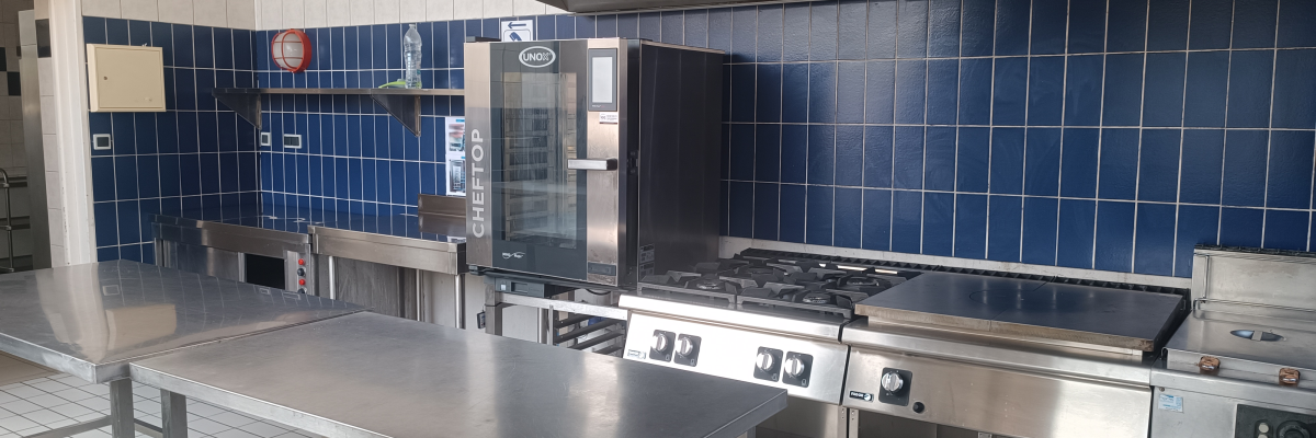 Cuisine avec plans de travail, plaques de cuisson, four, hottes, étagères et carrelage bleu.