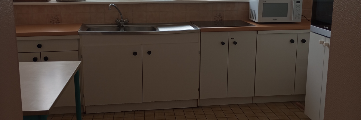 Cuisine avec meubles, table, évier, plaque de cuisson, micro-ondes et fenêtre.