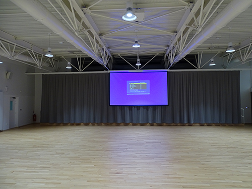 Salle vide avec écran, rideaux, projecteurs et parquet.