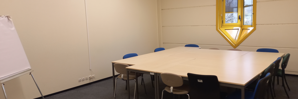 Salle de réunion avec table, chaises, tableau blanc et fenêtre.