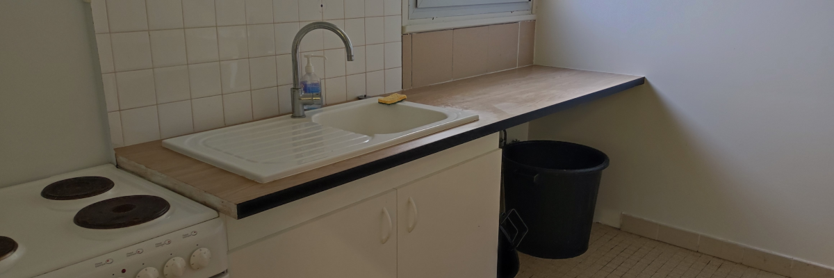 Cuisine avec évier, plan de travail, poubelle, cuisinière et fenêtre.